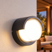 Round hood outdoor wall light beside a sheltered patio with timber seating