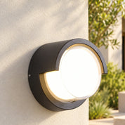 Round hood outdoor wall light on a rendered wall beside a green entry courtyard