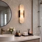 Warm vertical frosted wall sconce with dark side brackets above a marble bathroom vanity.