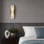 Vertical frosted wall sconce above a bed with gray headboard and teal bedding.