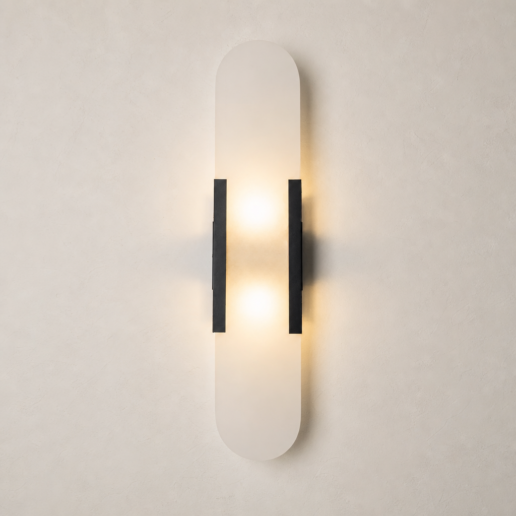 Vertical frosted wall sconce with black side brackets glowing warmly on a pale wall.