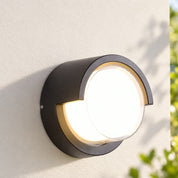 Round hood outdoor wall light on a pale garden wall in morning daylight