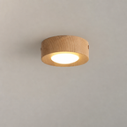 Round wooden ceiling light with a warm glowing diffuser on a plain ceiling.