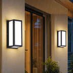 Black rectangular outdoor wall lights glow on a modern exterior wall in the rain.