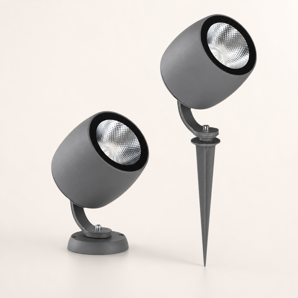 Two gray cylindrical outdoor spotlights with black rims and silver reflectors, one on a base and one on a ground spike.