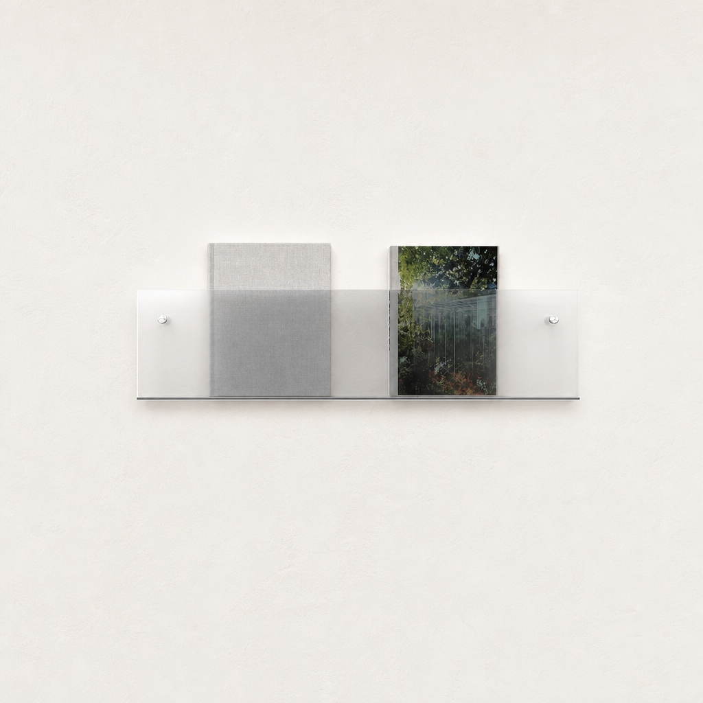 Clear wall-mounted acrylic display shelf holding two books on a white wall.