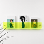 Neon lime acrylic wall shelf displaying three fashion magazines on a white wall.