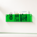 Transparent green wall-mounted magazine holder with publications inside on a white wall.