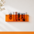 Orange translucent wall shelf holding magazines on a white wall.