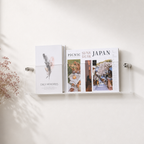 Clear acrylic wall-mounted shelf holding magazines and books with silver standoffs.
