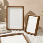 Three wooden photo frames with cream mats arranged on a light fabric surface.