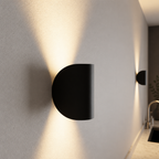 Black half-cylinder wall sconce casting warm light up and down on a textured white wall.