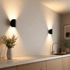 Two black wall sconces illuminate a modern kitchen counter with warm upward and downward beams.