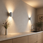Two white wall sconces cast warm up-and-down light over a minimalist kitchen counter.