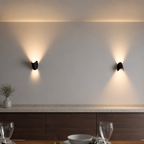 Two black wall sconces cast warm light above a wood cabinet and dining table.