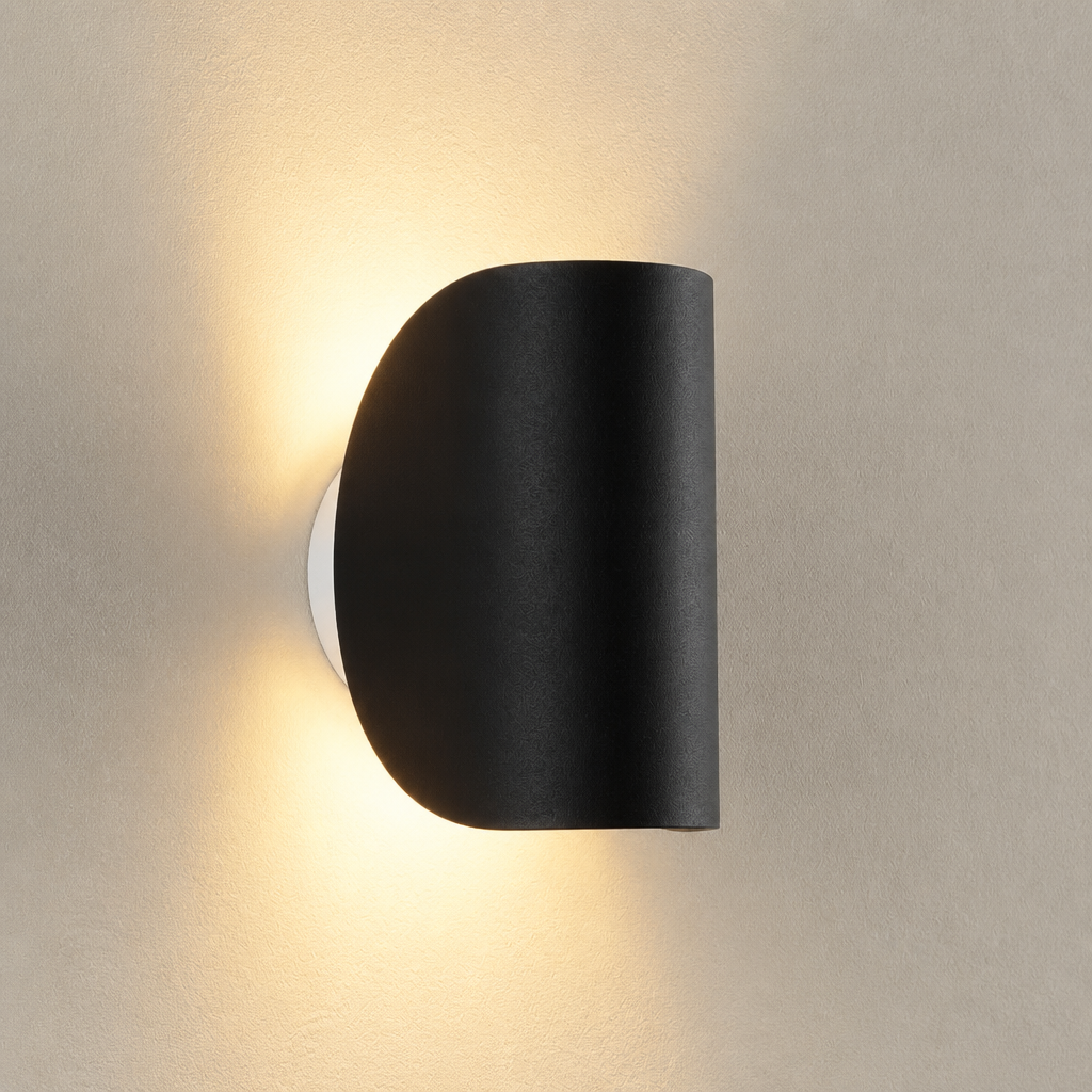 Black half-cylinder wall sconce casting warm light on a textured neutral wall.