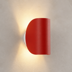 Red half-cylinder wall sconce on a textured pale wall casting a warm glow.