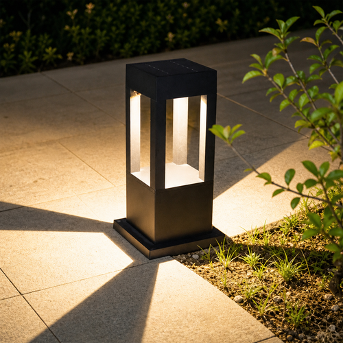 Black rectangular outdoor bollard light glowing warmly beside a garden path.
