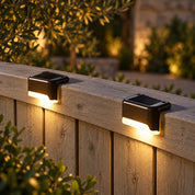 Compact solar fence lights casting a warm glow down a pale timber fence.
