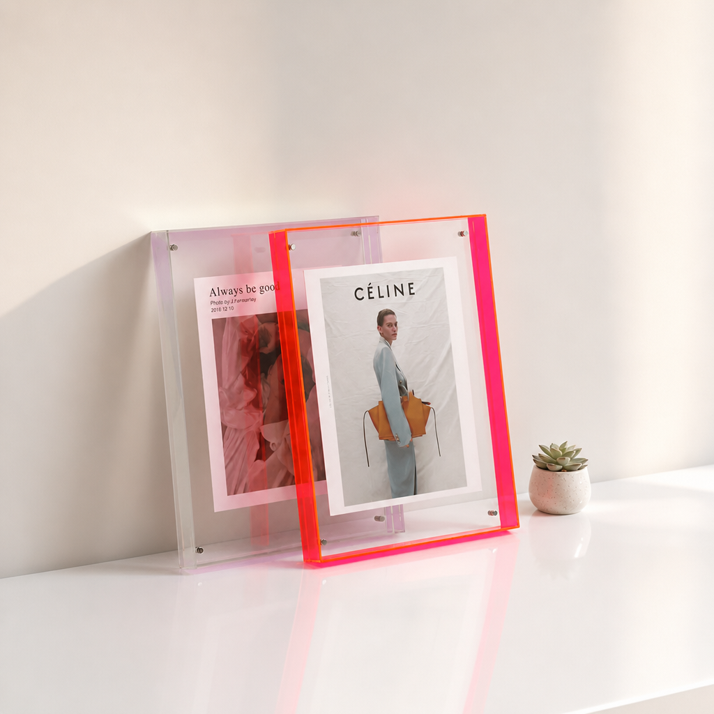 Neon pink acrylic photo frame holding fashion prints on a glossy white shelf.