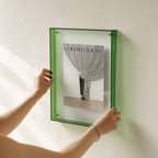 Green transparent wall frame displaying The Kinfolk Home book, held by two hands.