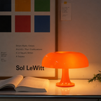Glossy orange mushroom table lamp glowing on a desk beside an open book.