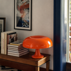Glossy orange mushroom table lamp on a wooden table beside stacked books.