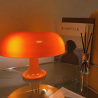 Glossy orange mushroom table lamp on a reflective surface beside books and a reed diffuser.