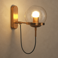 Brass wall sconce with clear glass globe and black hanging cord glowing warmly.