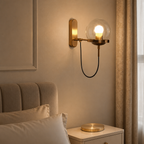 Brass wall sconce with a glowing glass globe above a bedside table.