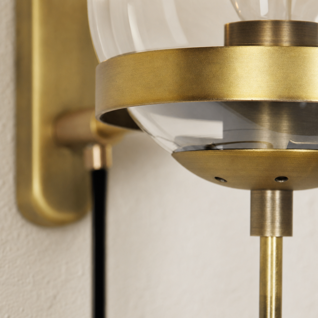 Close-up brass wall sconce with clear glass shade and black support rod.
