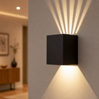 Black cube wall sconce casting warm geometric light beams on a neutral wall.