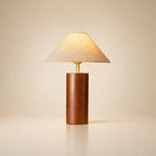 Wooden table lamp with beige fabric shade and brass neck on a plain warm background.