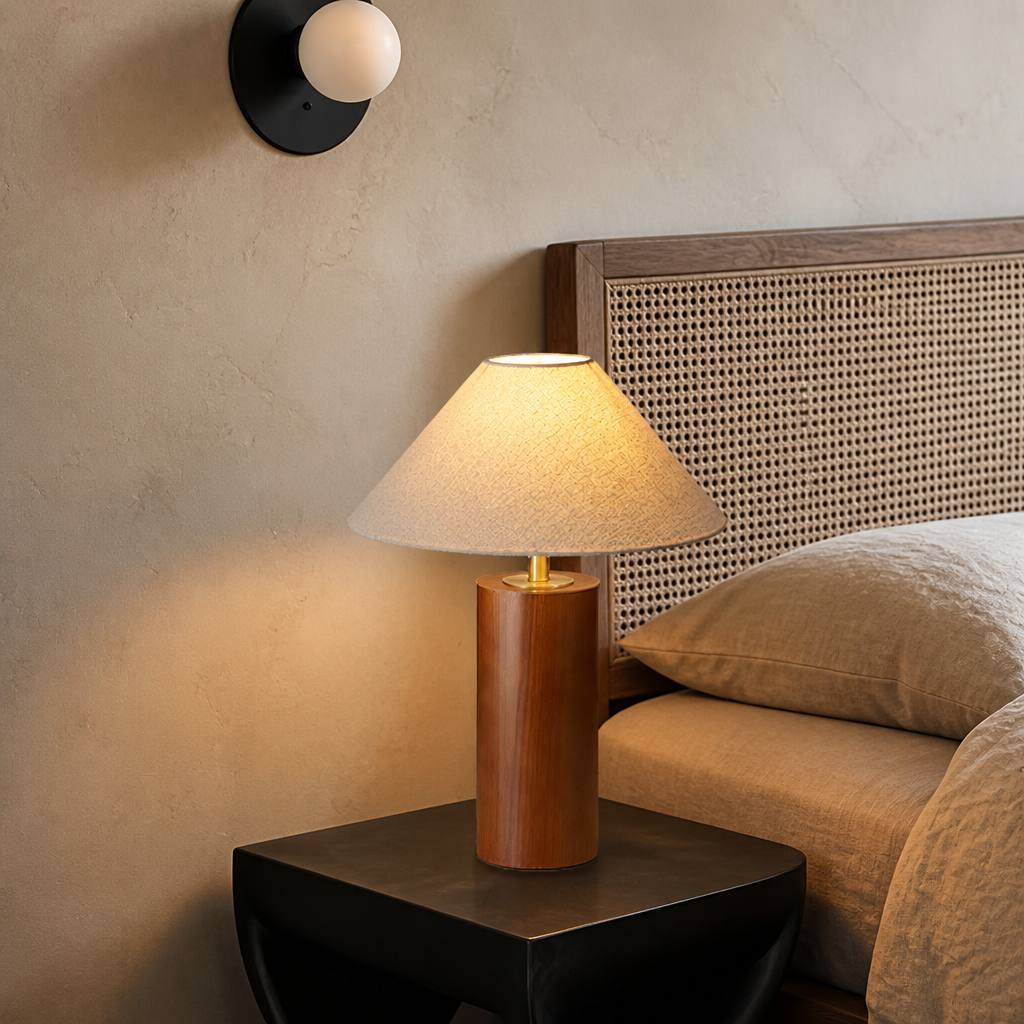 Wooden cylinder table lamp with beige shade on a black bedside table.