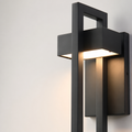Black rectangular wall sconce with warm light glowing against a pale wall.