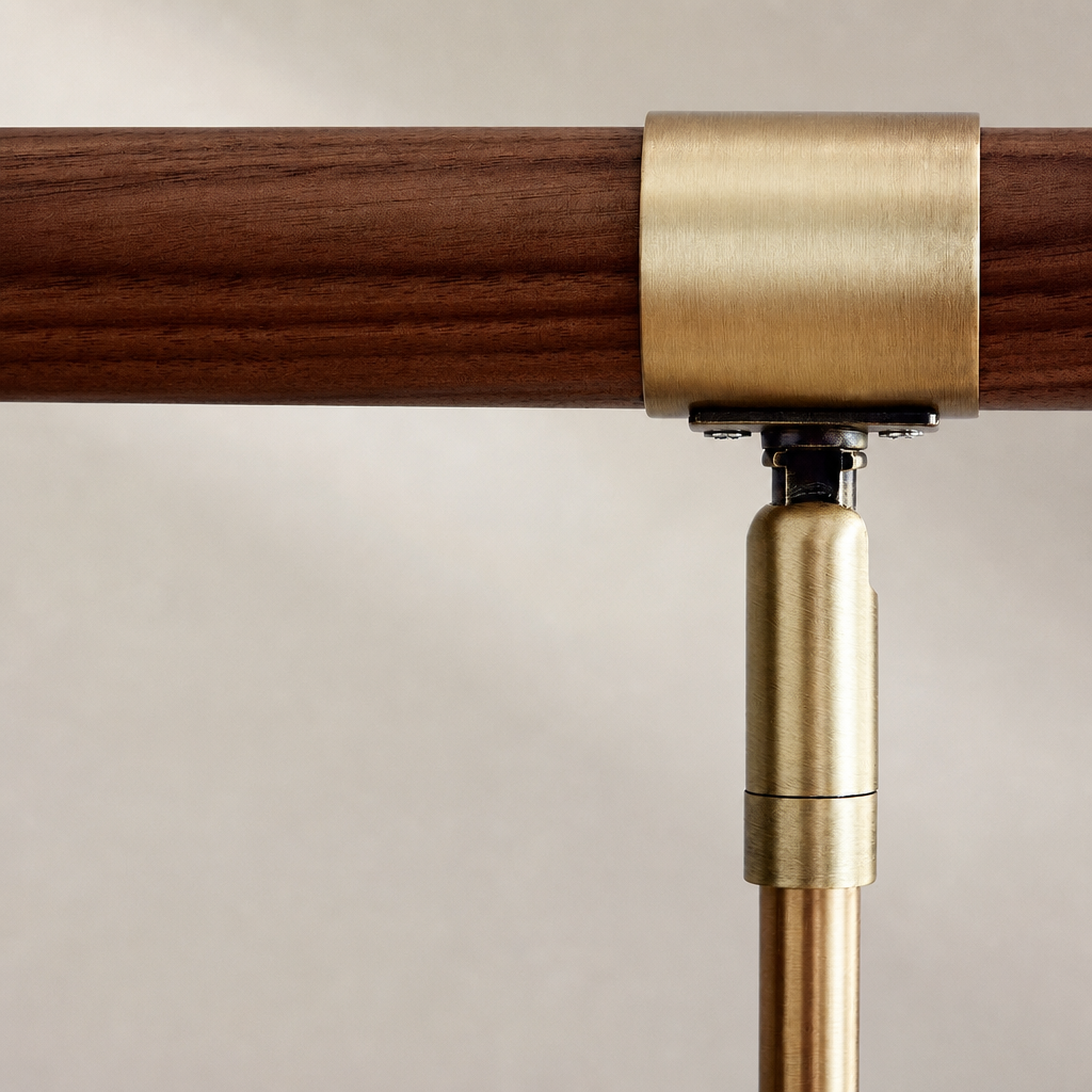 Brushed brass railing bracket clamping a dark wooden handrail against a pale wall.