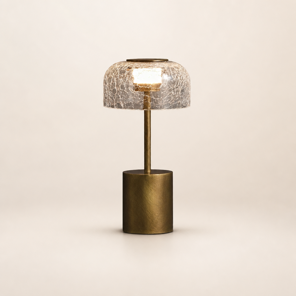 Brass table lamp with crackled glass dome shade glowing on a pale neutral background.