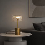 Brass table lamp with glowing crackle glass shade on a white round side table.
