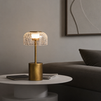 Brass table lamp with a glowing crackle glass shade on a white side table.