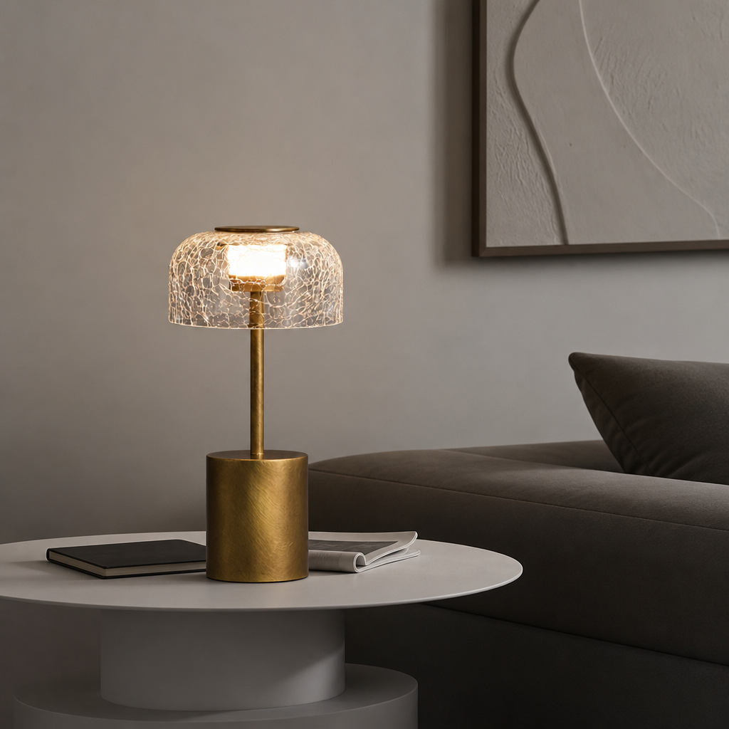 Brass table lamp with a glowing crackle glass shade on a white side table.