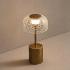 Gold table lamp with a cracked clear glass shade glowing warmly on a gray surface.