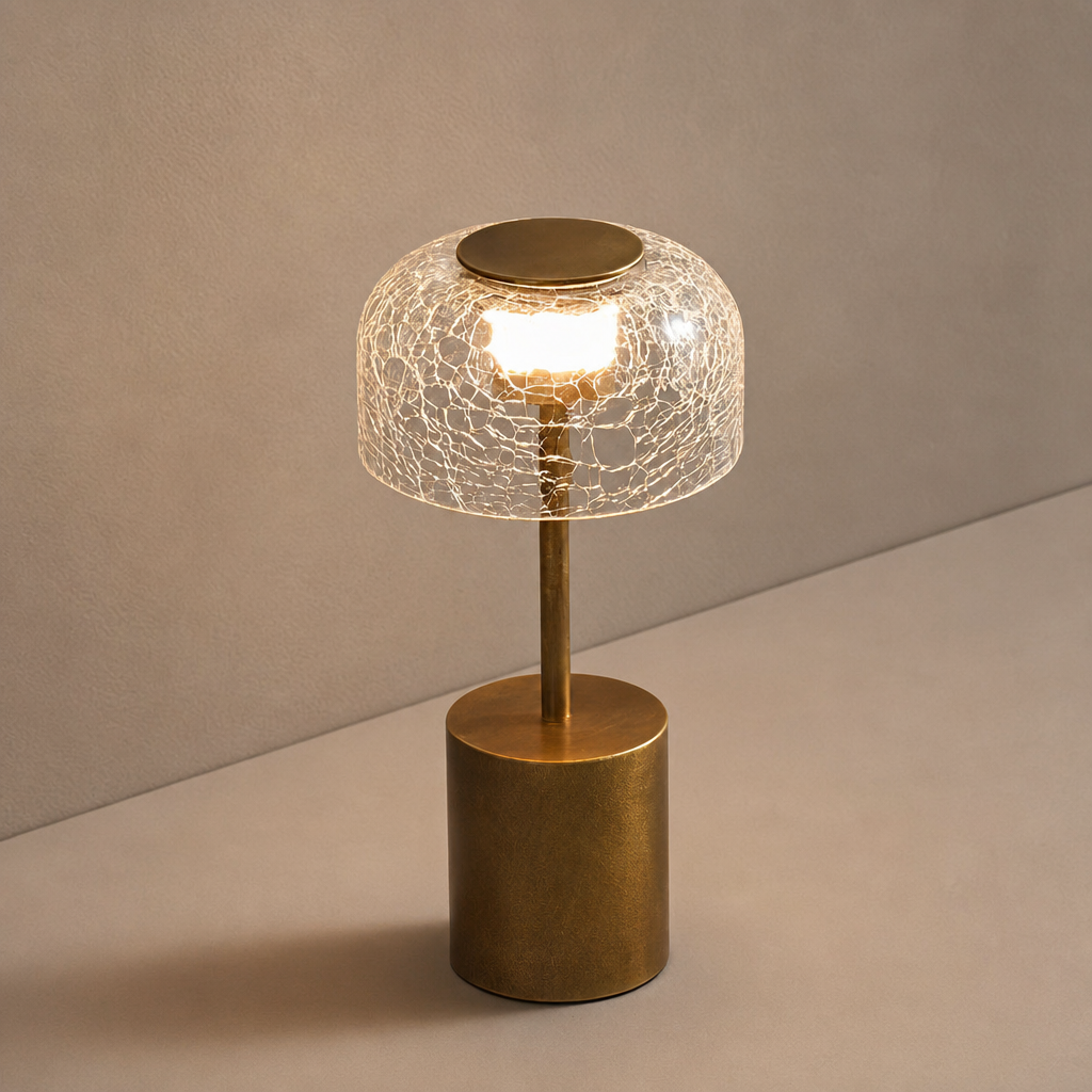 Gold table lamp with a cracked clear glass shade glowing warmly on a gray surface.