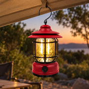 Red lantern suspended by its hook beneath a camping shelter.