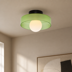 Green flush mount ceiling light with translucent shade and glowing round bulb.