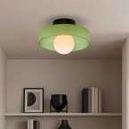 Green flush mount ceiling light with black base and glowing white globe above a neutral shelf.