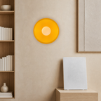 Orange circular wall light above a white textured speaker in a warm minimalist room.