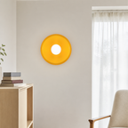 Yellow circular wall lamp with a white center mounted on a light living room wall.