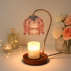 Pink glass flower warmer lamp melting a glowing white candle on a wooden base.