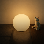 Glowing spherical lamp on a tiled floor beside a small white cat figurine.