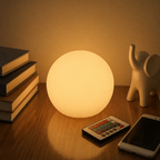 Glowing spherical lamp on a wooden table beside books, a remote, a phone, and a small elephant figurine.